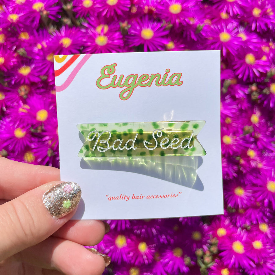 hand holding eugenia bad seed hair clips in front of fuchsia flowers with color camp nails